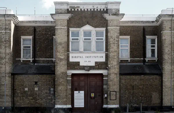 Historic yellow brick institutional building with symmetrical Georgian architecture, featuring the inscription BORSTAL INSTITUTION 1908 above double wooden entrance doors, with white-framed sash windows and decorative stone elements.
