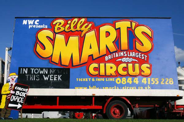 A large circus advertisement billboard on the side of a truck or trailer. The colorful sign reads “Billy Smart’s Circus” with “Britain’s Largest Circus” underneath, advertising that it’s “In Town This Week” with ticket and contact information displayed.
