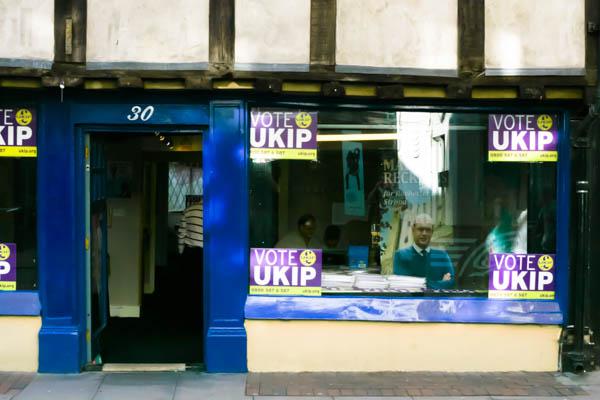 A UKIP (UK Independence Party) campaign office with purple and yellow branding. Multiple VOTE UKIP signs are visible in the windows, and there appears to be campaign staff or volunteers inside the office space. The storefront has the characteristic UKIP color scheme and messaging
