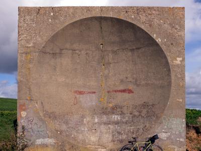 At Abbot's Cliff (Langdon Cliffs) between Folkstone and Dover. A pre-radar sound mirror (listening ear). It was cast in July 1928. The purpose was to provide an early warning against enemy aircraft. It is 20 foot in diameter. Concrete acoustic mirror with a bicycle leaning against it in a rural field.