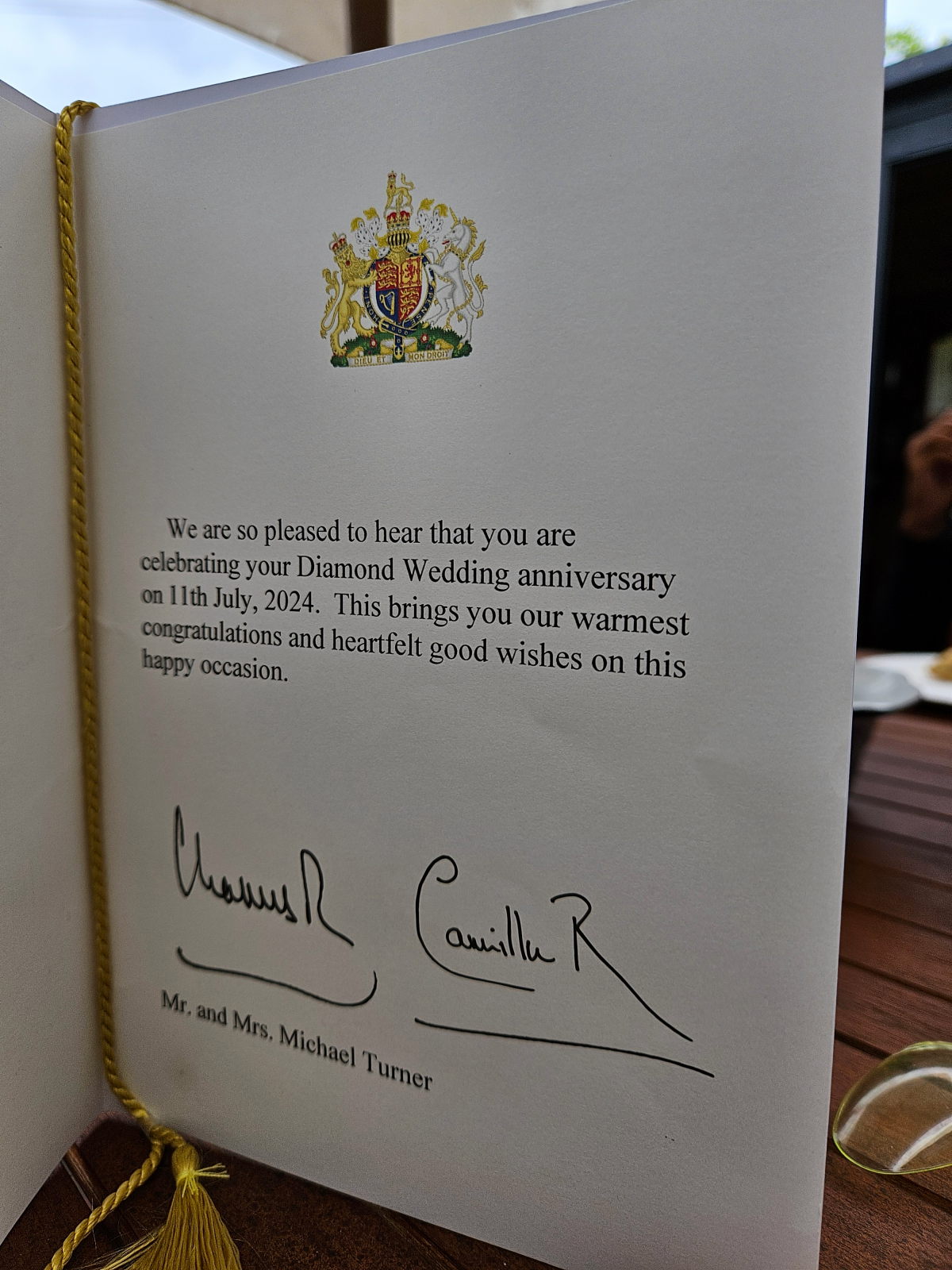 We are so pleased to hear that you are celebrating your Diamond Wedding anniversary on 11th July, 2024. This brings you our warmest congratulations and heartfelt good wishes on this happy occasion. The letter is signed by the Charles and Camilla, with handwritten signatures above printed text that reads Mr. and Mrs. Michael Turner. The document appears to be an official royal congratulations letter for a couple celebrating their 60th wedding anniversary Diamond Wedding anniversary. The Royal Coat of Arms features the traditional heraldic symbols including a lion and unicorn as supporters, with a crown at the top and the motto Dieu et mon droit visible on a banner at the bottom of the coat of arms.