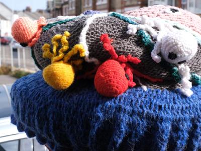 The side view shows a postbox topper with a knitted marine scene, including a colorful octopus and various small, crocheted sea creatures in red, yellow, white, and grey.
