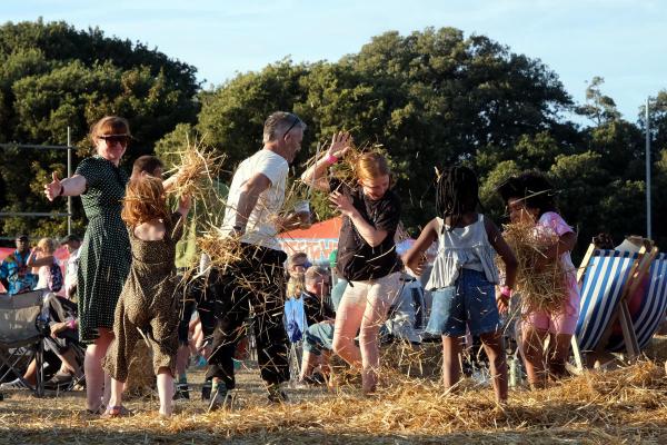 A group of children joyfully playing in a pile of hay during a lively outdoor festival.