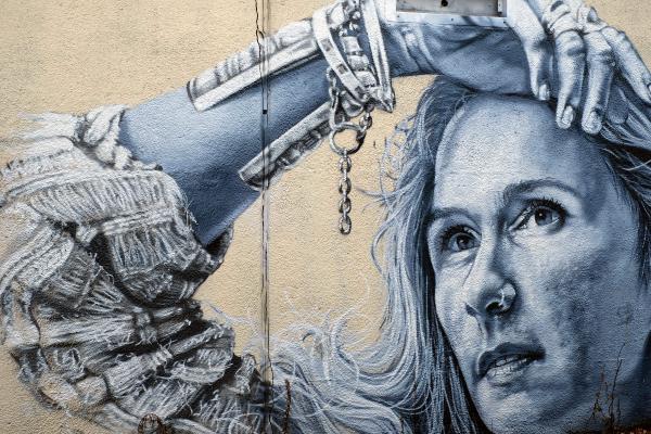 Close-up of a lifelike grayscale mural of a woman gazing upward, her hair rendered in fine brush-stroke detail, against a pale textured wall.