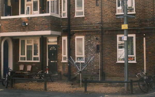Red-brick terraced houses on Whiston Road, Hackney, with bicycles and chairs behind a low metal railing outside a black front door.