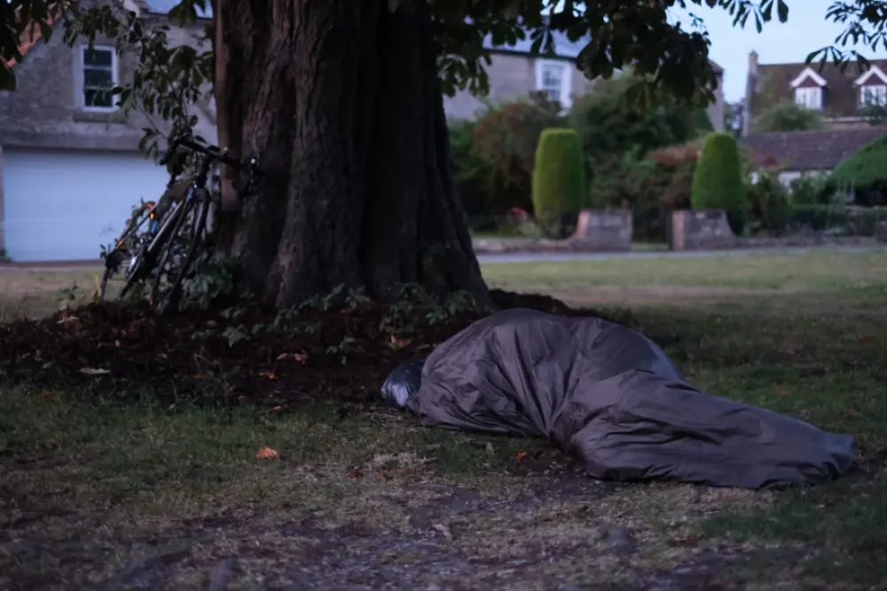An occupied bivvy bag beneath a tree. A bicycle is propped up against the tree.